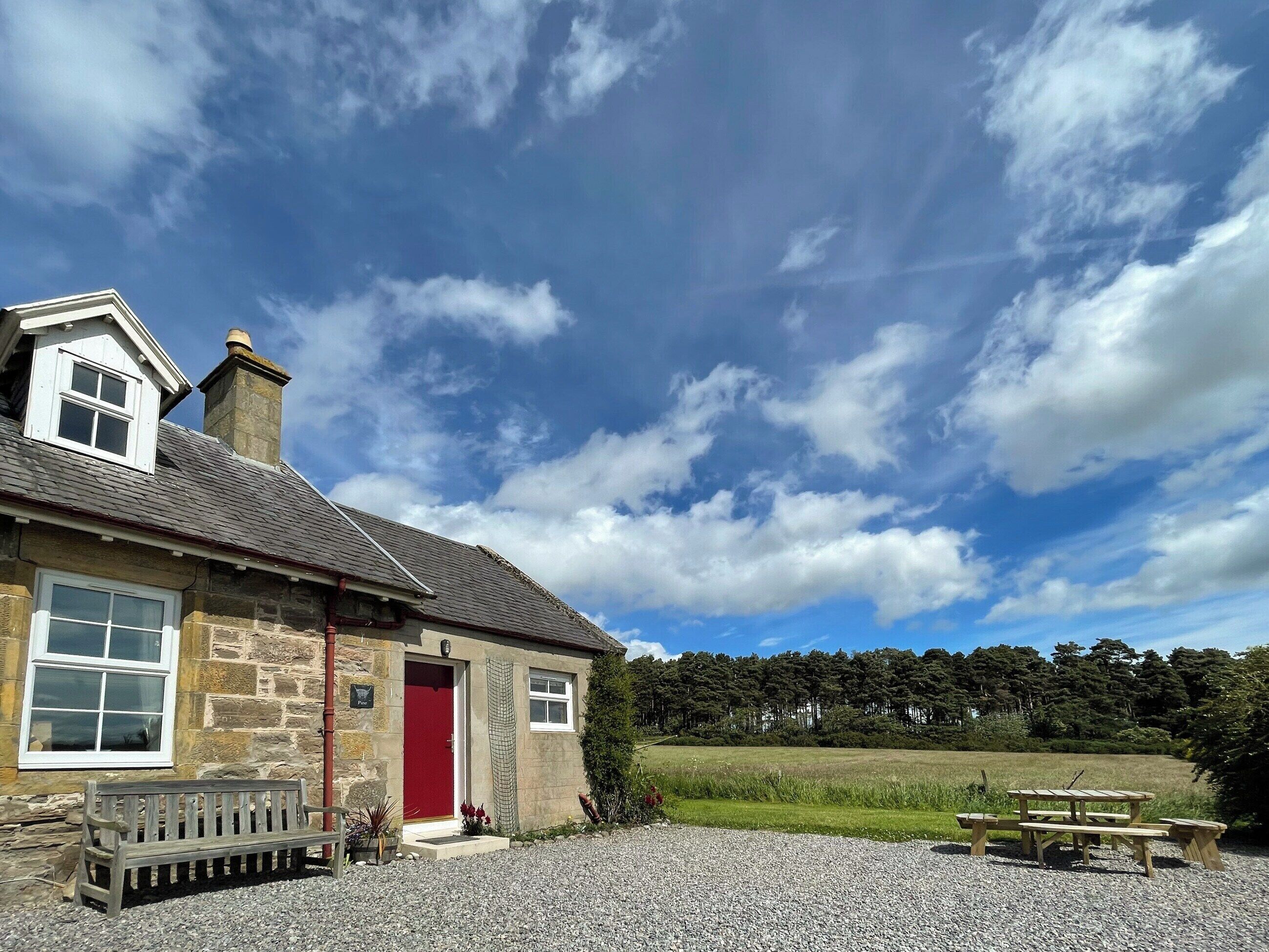 A stone building with a red door, a bench, and a picnic table in front.