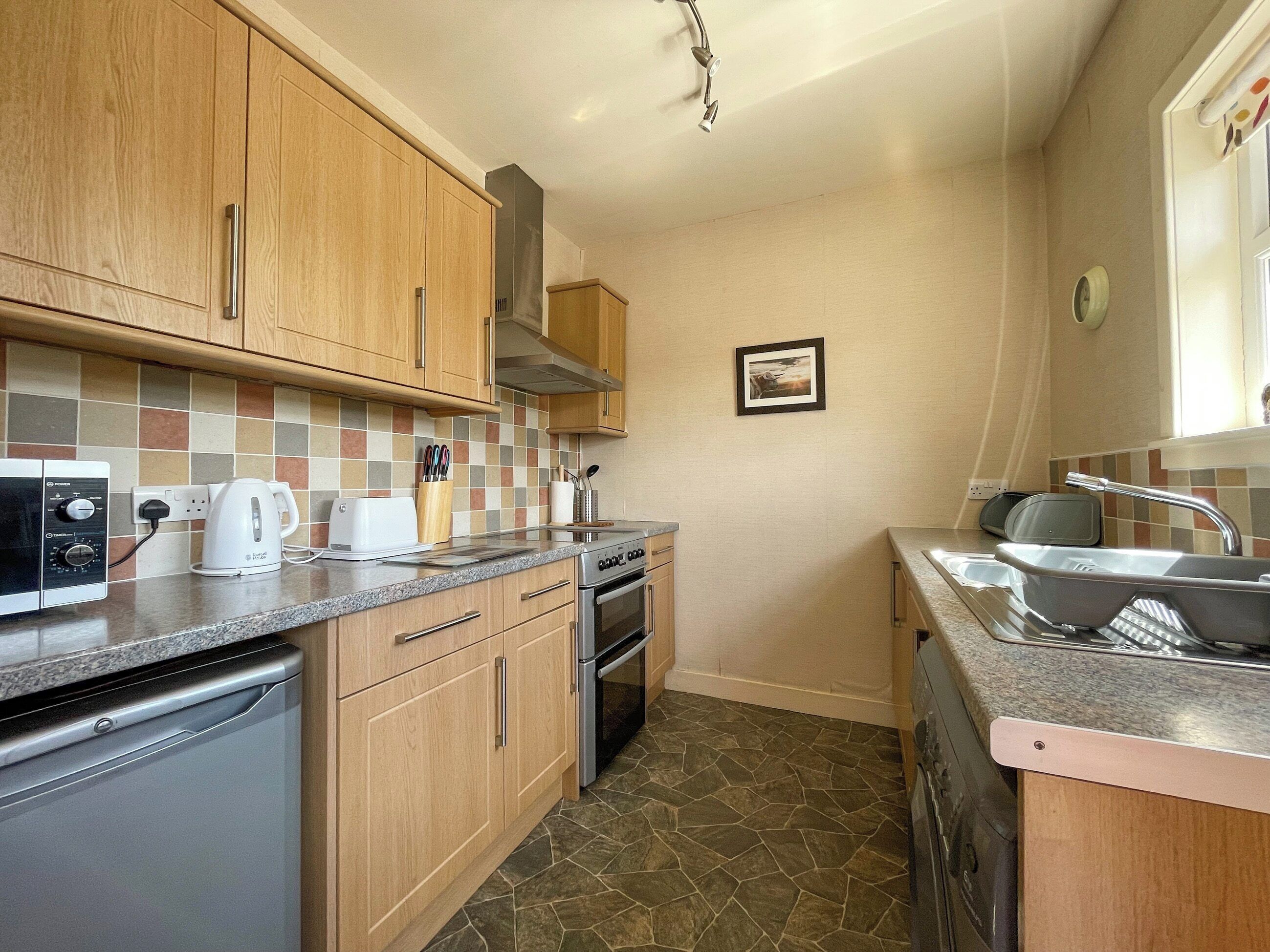 A compact kitchen with wooden cabinets, a microwave, a toaster, and a sink.