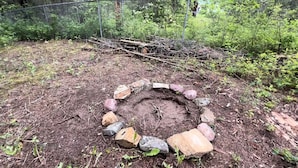 A circular stone fire pit surrounded by rocks in a wooded area.