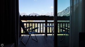 A balcony with two chairs and a small table, overlooking a mountainous landscape.