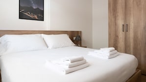 A neatly made bed with white linens and towels, a wooden headboard, and a nightstand with a lamp.