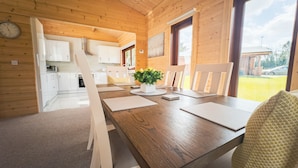 En stuga med träpanel på insidan, med ett matbord för fyra personer, ett köksområde och utsikt över naturen.
