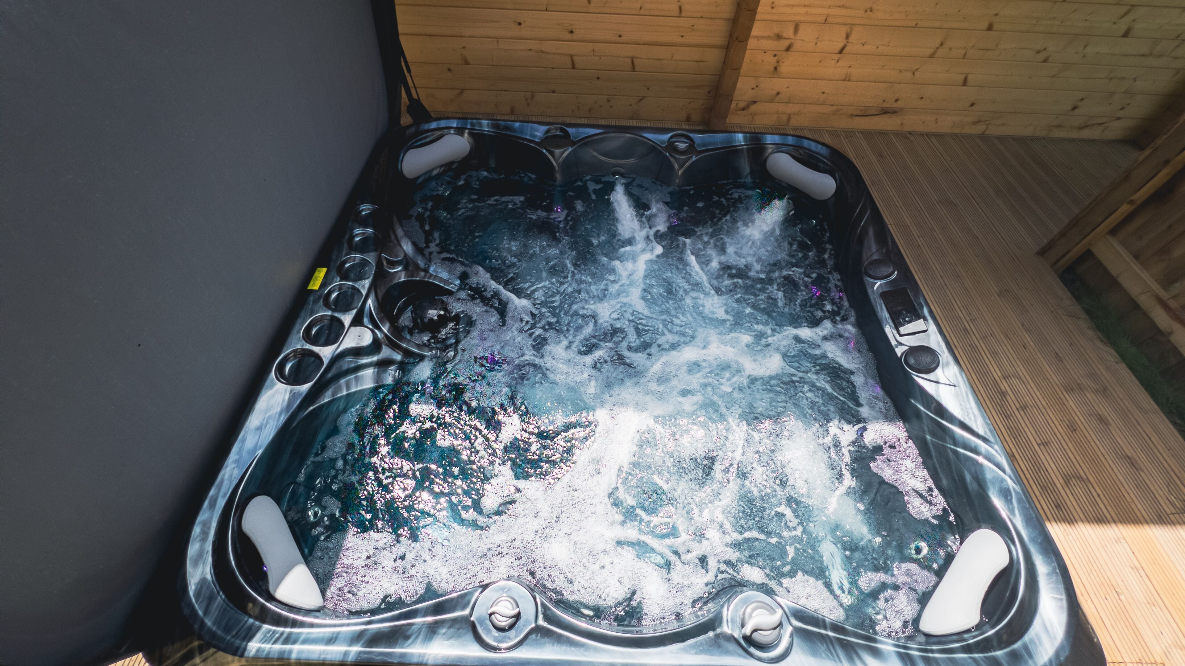 Un bain à remous doté de plusieurs jets, d’un panneau de commande et d’un plancher en bois qui l’entoure.