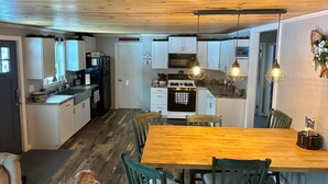 A modern kitchen with white cabinets, a wooden dining table, and pendant lighting. - Newly Renovated, perfectly located and fully equiped. (Portage Lake)