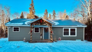 A two-story house with a metal roof, a front porch with a wooden railing, and a Christmas wreath on the door. - Newly Renovated, perfectly located and fully equiped. (Portage Lake)