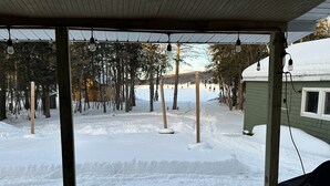 A covered outdoor area with a snow-covered ground, wooden posts, and a view of a building with a window. - Newly Renovated, perfectly located and fully equiped. (Portage Lake)