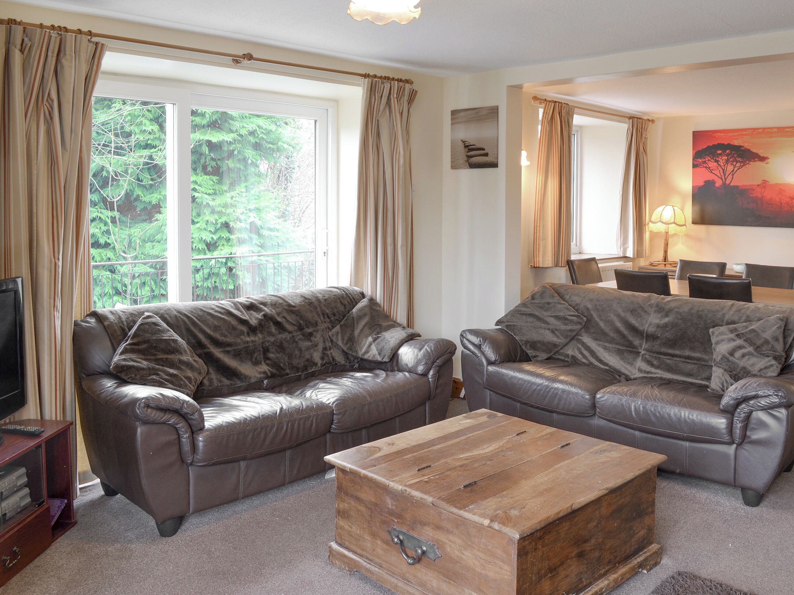 Ein Wohnzimmer mit zwei Ledersofas, einem Holztisch, einem Fernsehschrank und einem Esstisch mit Stühlen.