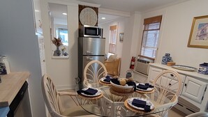 A dining area with wicker chairs and a glass table, a kitchen with a microwave and refrigerator, and a white interior. - FALL 2026 Gorgeous Renovation-Walk to Beach, Asbury, Pets Welcome! (Neptune Township)