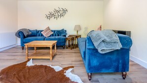 Ein modernes Wohnzimmer mit einem blauen Sofa, einem Holztisch und einem Kuhfellteppich.