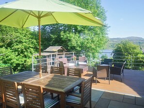 Une terrasse avec des tables et des chaises en bois, un parasol jaune et une vue sur un lac et des collines.