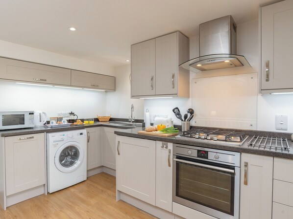 A modern kitchen with a built-in washing machine, an oven, and a microwave. - 2 bedroom accommodation in Fowey (Fowey)