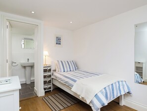 A bedroom with a single bed, a bedside table with a lamp, a small bedside shelf, and a mirror.