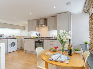 A modern kitchen with a dining area, including a table set for two with a wine glass, a vase with flowers, and a bottle of wine.