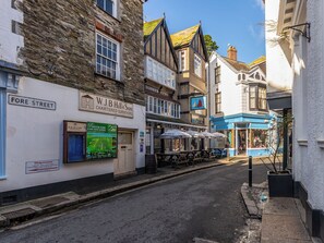 A narrow street lined with traditional buildings, including a chartered surveyors office and a shop with outdoor seating.