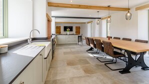 Een moderne keuken met een groot eiland, een eethoek met een houten tafel en stoelen, en een aan de muur bevestigde televisie.