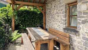 Ein Gartenmöbel-Set aus Holz mit Bank und Tisch vor einer Steinmauer, umgeben von Grünpflanzen.