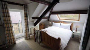 Een slaapkamer met een schuine plafond, een houten bed, een nachtkastje, een lamp en een raam met gordijnen.