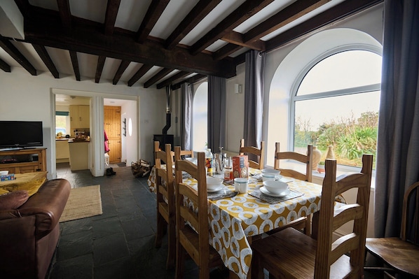 A dining area with a table set for four, wooden chairs, and a view through large windows.