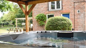 Un jacuzzi bajo una pérgola de madera, con un edificio de ladrillo al fondo.
