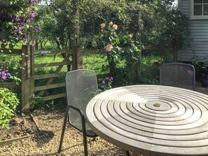 A round table with concentric circles, two metal chairs, a wooden fence, and a garden with flowers and greenery. - Fig Tree Shepherds Hut (Bridport)