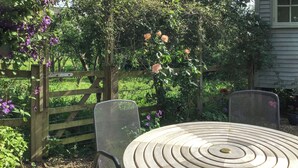 A round table with concentric circles, two metal chairs, a wooden fence, and a garden with flowers and greenery. - Fig Tree Shepherds Hut (Bridport)