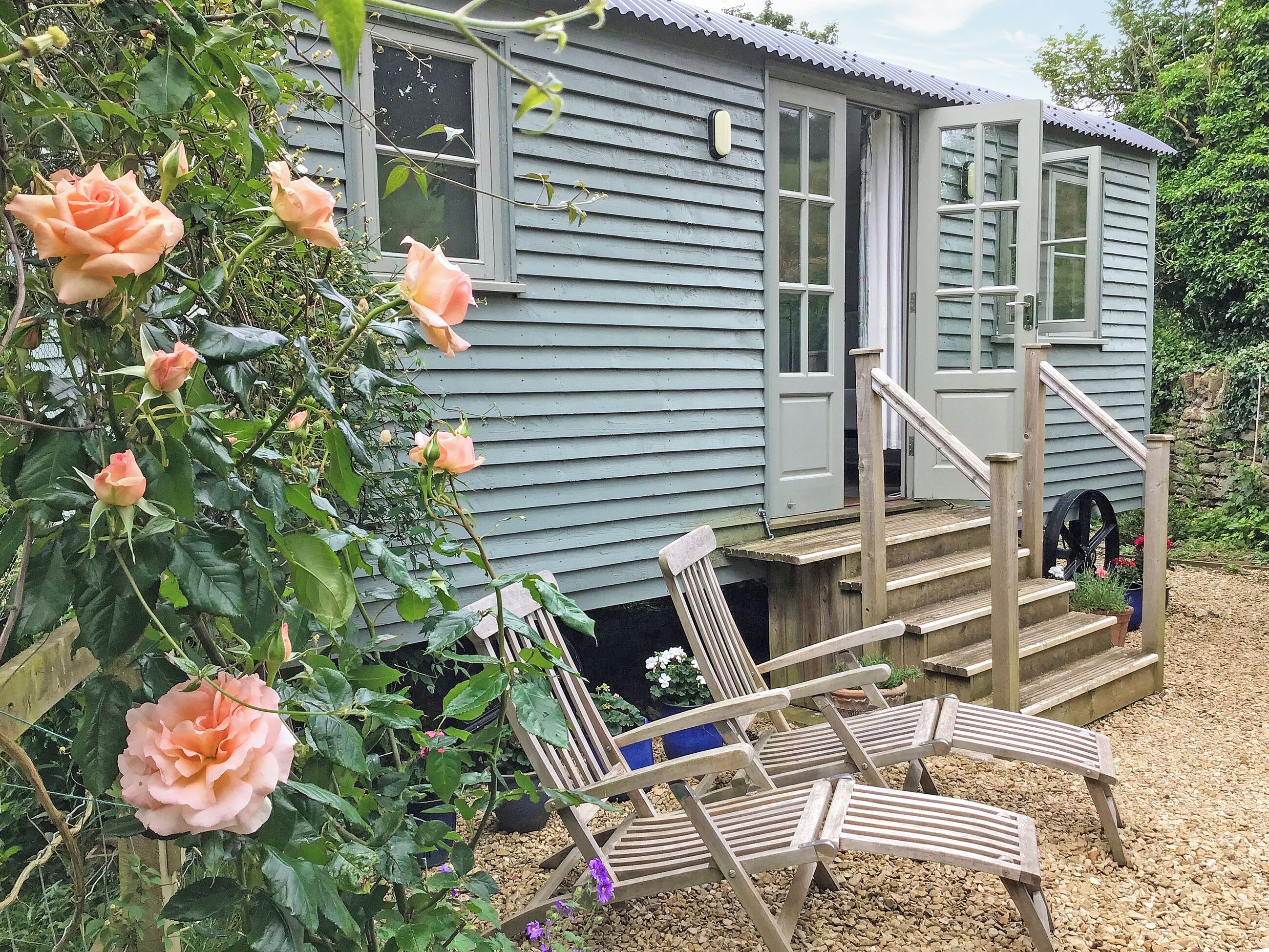 A small house with a porch, wooden chairs, and a rose bush.