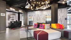 A modern hotel lobby with a reception desk, seating area with colorful cushions, and patterned walls. - Aloft by Marriott Atlanta Perimeter Center (Atlanta)
