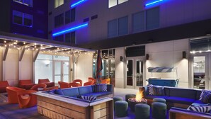 An outdoor seating area with wooden furniture and orange chairs, a fire pit, and string lights. - Aloft by Marriott Atlanta Perimeter Center (Atlanta)
