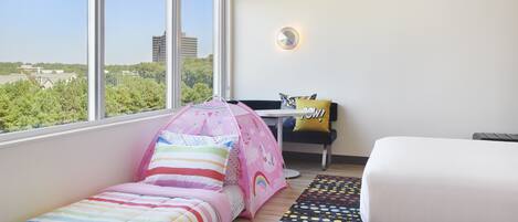 Ein Schlafzimmer mit Bett, Schreibtisch und Fenster mit Blick auf Gebäude und Bäume.