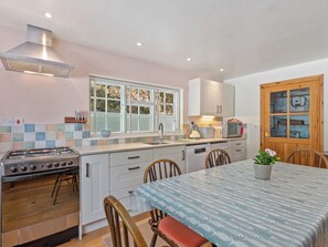 A kitchen with a stove, sink, and dining area with chairs and a table.