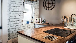 Et køkken med murstensvæg, træbordplade, sort komfur og et stort ur.