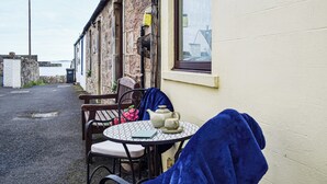 Et lille udendørs opholdsområde med et bord, stole, et vindue og en stenvæg.