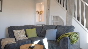 Ein Wohnzimmer mit einem dunkelgrauen Sofa, einem Holztisch und einer Treppe mit weißen Geländern.