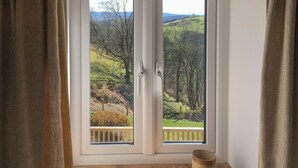 Ein Zimmer mit einer großen Schiebetür, die auf einen Balkon mit Blick auf eine hügelige Landschaft führt.