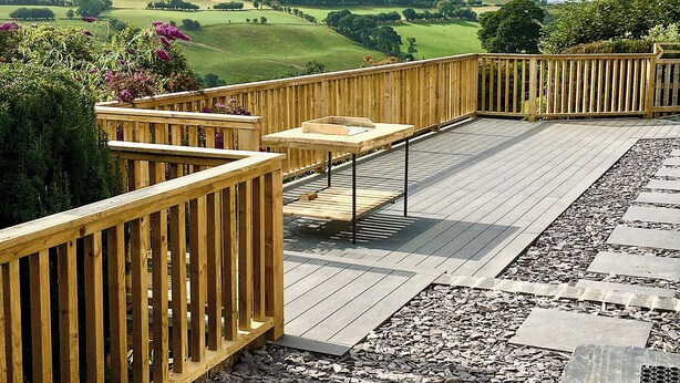 Eine Holzterrasse mit Tisch und Stühlen, umgeben von einem Kiesweg und Blick auf sanfte Hügel.