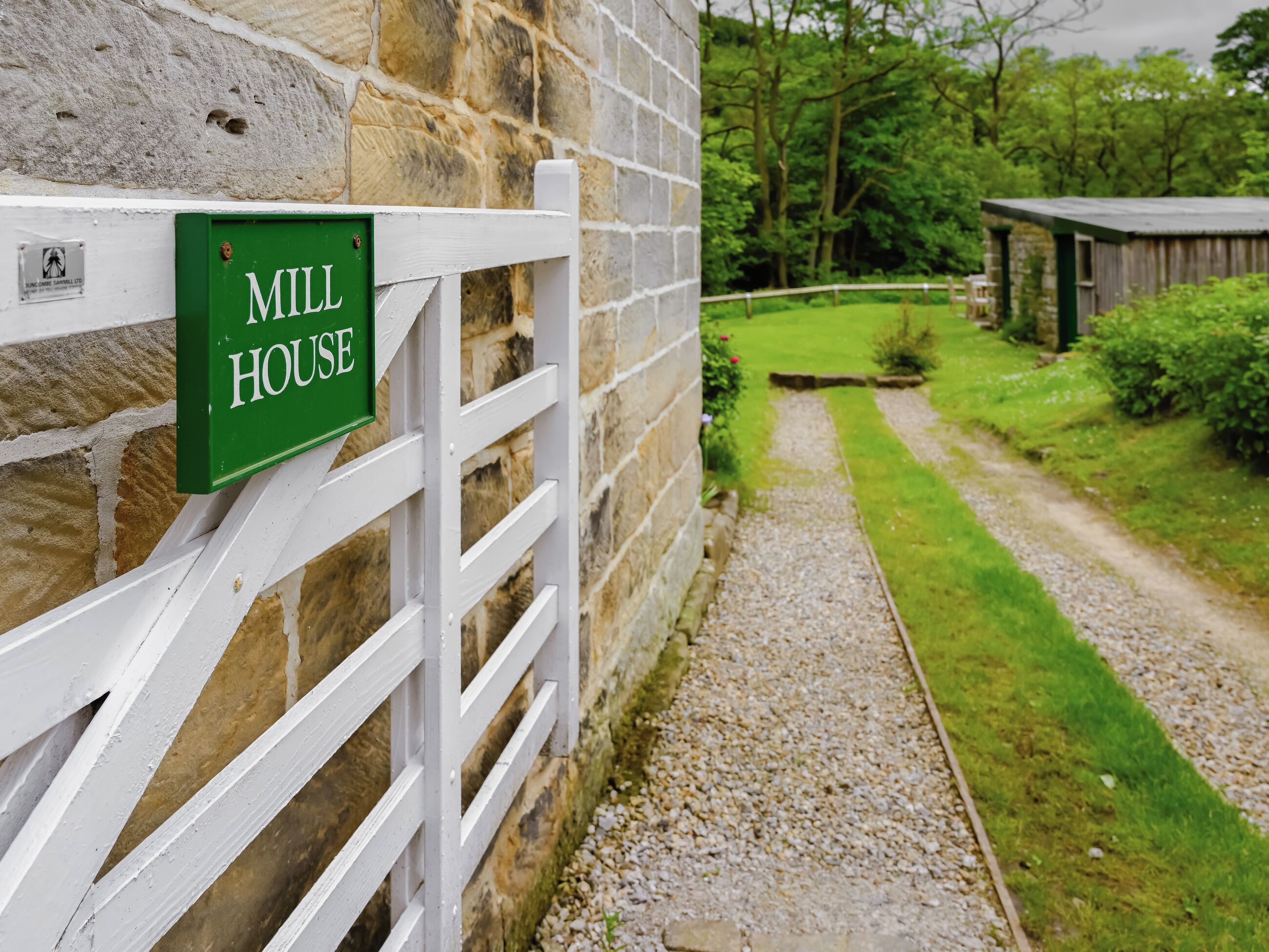 A stone wall with a white gate and a green sign that reads 'MILL HOUSE.'
