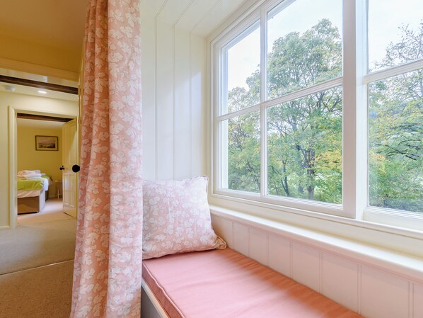 Ein Zimmer mit Fenster, Bett, Tür und Blick auf Bäume.