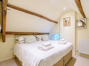 Un dormitorio con techo inclinado, cama con ropa blanca, almohadas con motivos florales y un radiador.