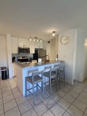 Una cocina moderna con una isla central, electrodomésticos de acero inoxidable y un reloj en la pared.