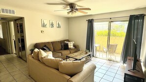 Ein Wohnzimmer mit einer Couch, einem Couchtisch und einem Deckenventilator. Eine Glastür führt zu einem Außenbereich.