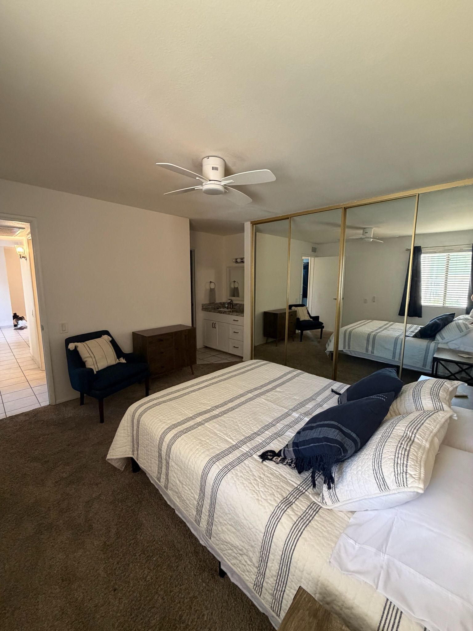 A bedroom with a bed, a dresser, a chair, a mirror, and a ceiling fan.