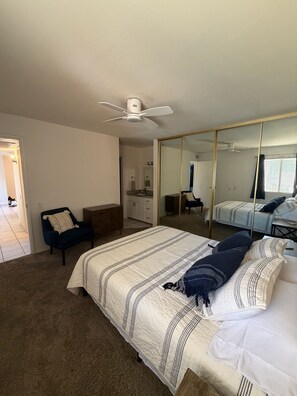 Ein Schlafzimmer mit einem Bett, einem Schminktisch, einem Sessel, einem Spiegel und einem Deckenventilator.
