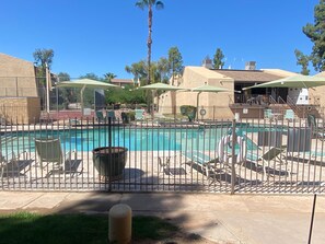 Una piscina con zona vallada, sillas de descanso y sombrillas.