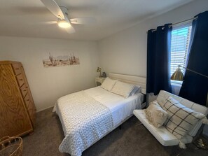 Une chambre à coucher avec un lit, une table de chevet, une lampe, une fenêtre avec des rideaux et une armoire en bois.