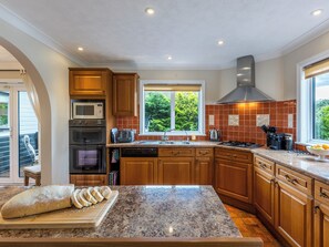 Une cuisine avec des meubles en bois, un plan de travail en granit, un four à micro-ondes, une cuisinière et une fenêtre donnant sur un paysage verdoyant.