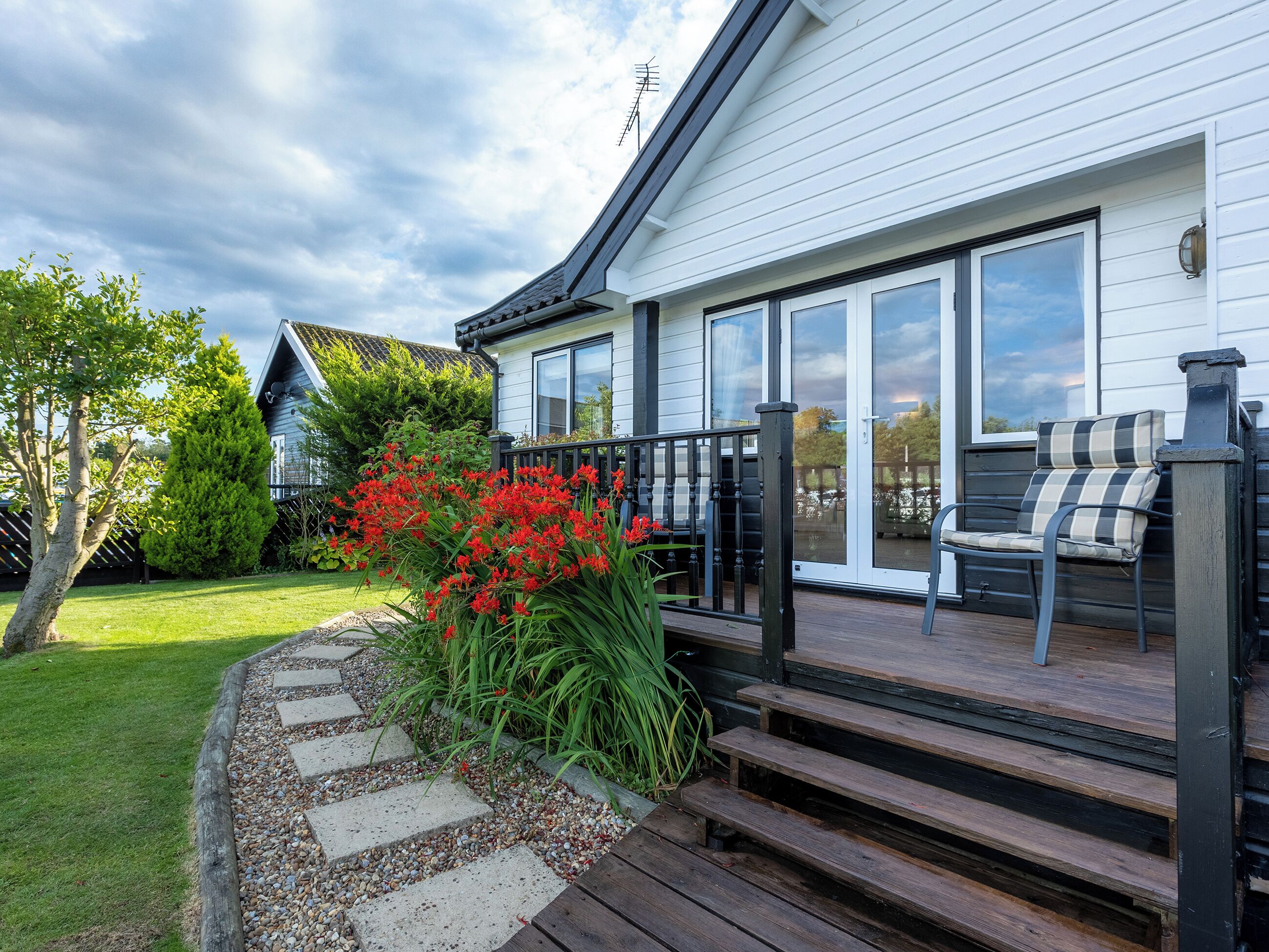 A house with a deck, a garden with red flowers, and a clear sky.