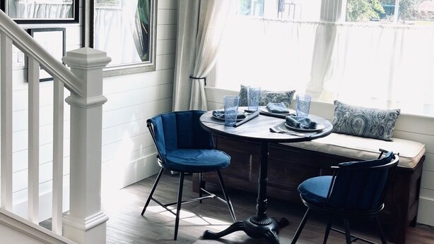 A dining area with a round table, two blue chairs, and a bench. There is a staircase with white railings and a black pendant light above the table. - "Bee Keeper's Cottage" on private estate, new construction, close to everything! (Sarasota)