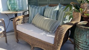 A wicker sofa with striped cushions, a round table with glass bottles, and a potted plant. - "Bee Keeper's Cottage" on private estate, new construction, close to everything! (Sarasota)
