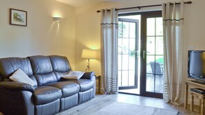 A living room with a leather sofa, a TV, a lamp, and a view through a glass door.