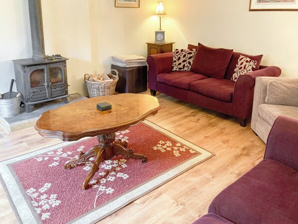 A cozy living room with a wooden table, a red sofa, a beige armchair, a fireplace, and a lamp on a side table.